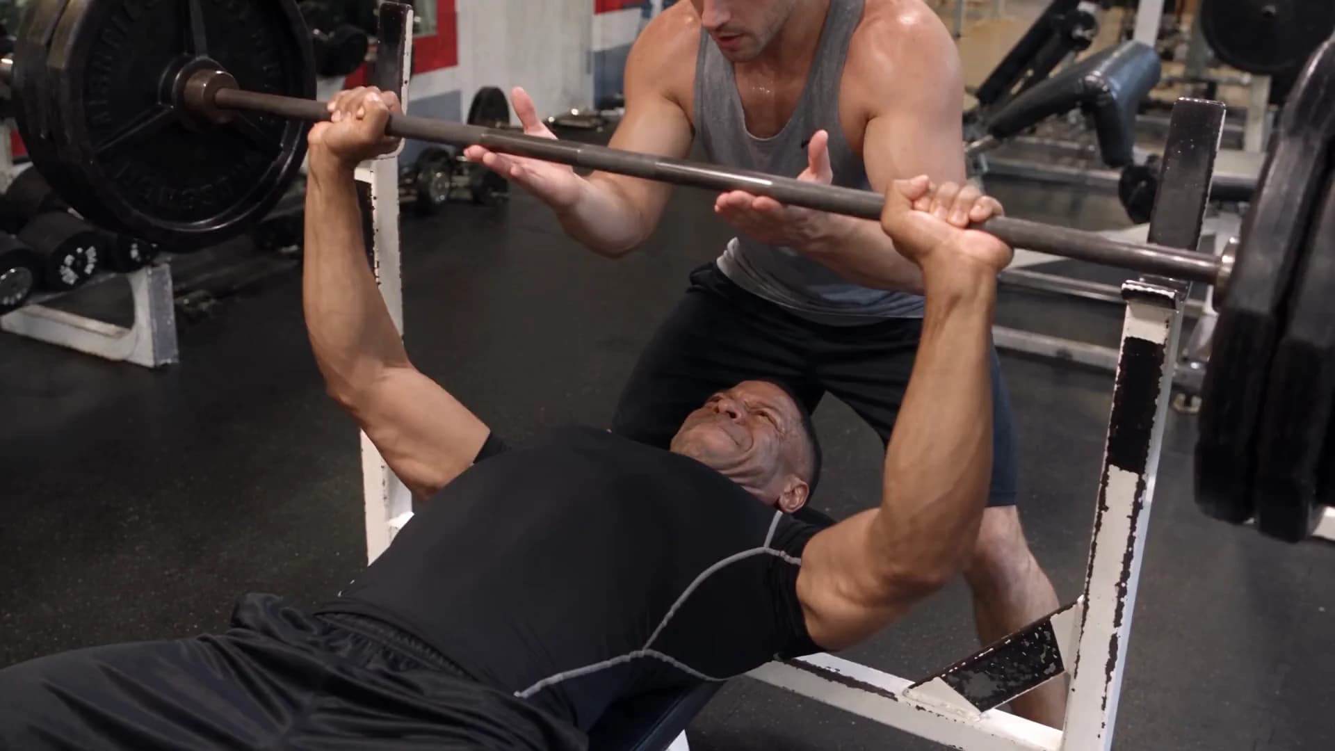 A man bench pressing with a spotter, the training that feeds his Omnis Report.